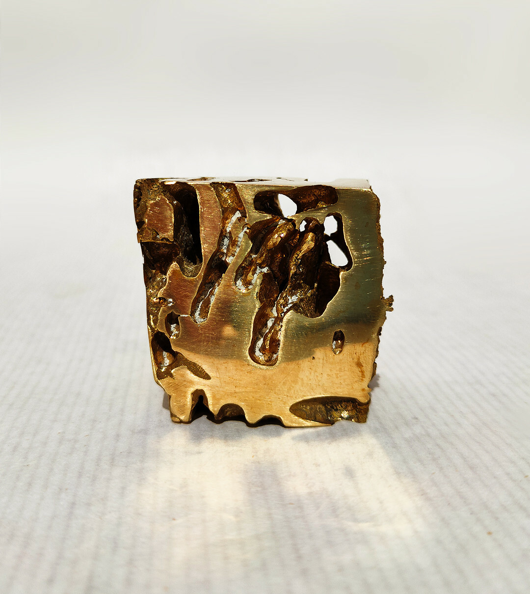 Frontal view of the brass cube, showing only one side, you can see through the piece because the tunnels cut holes that go through the whole piece