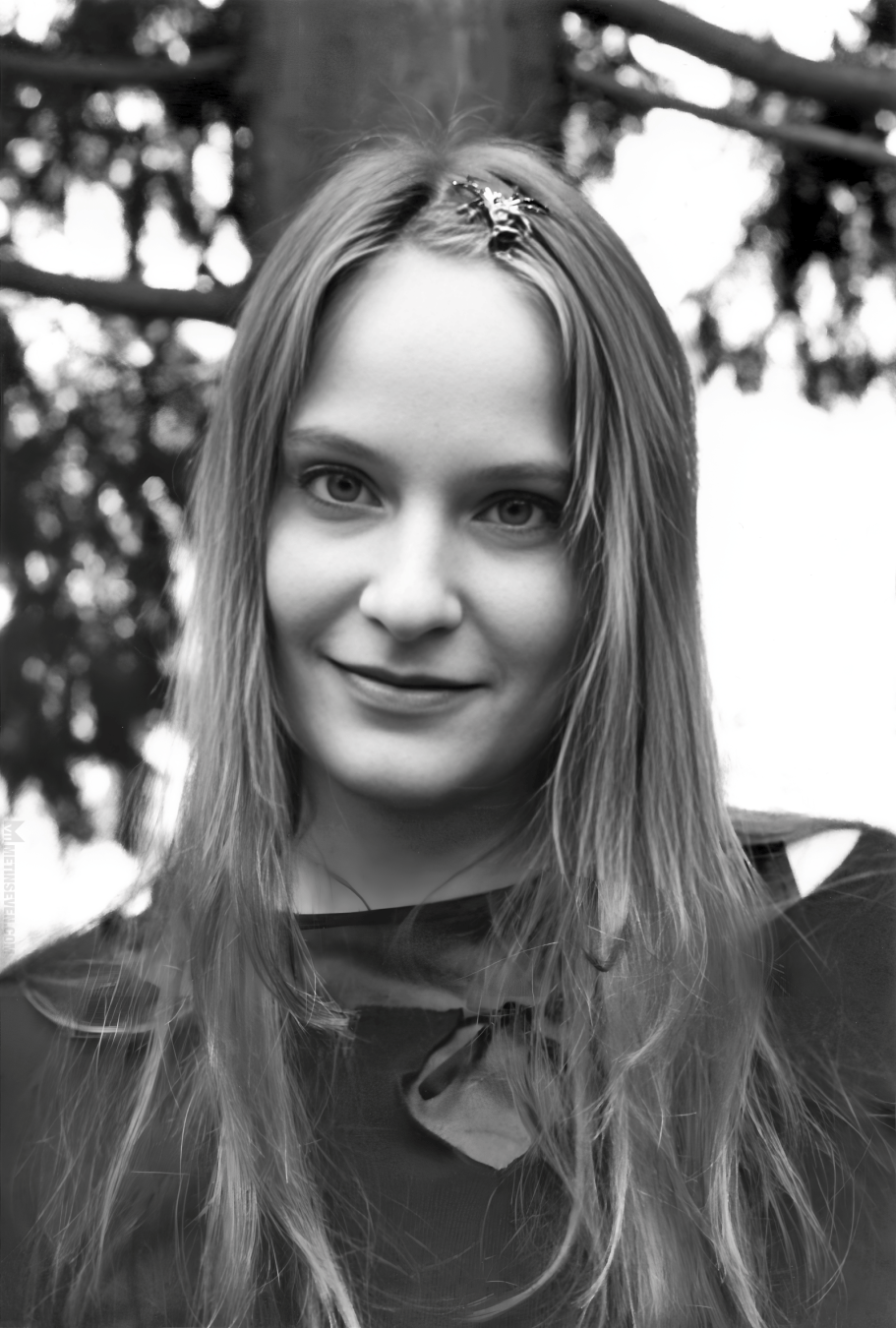 Black and white photograph of a young woman standing in front of a tree that's out of focus.