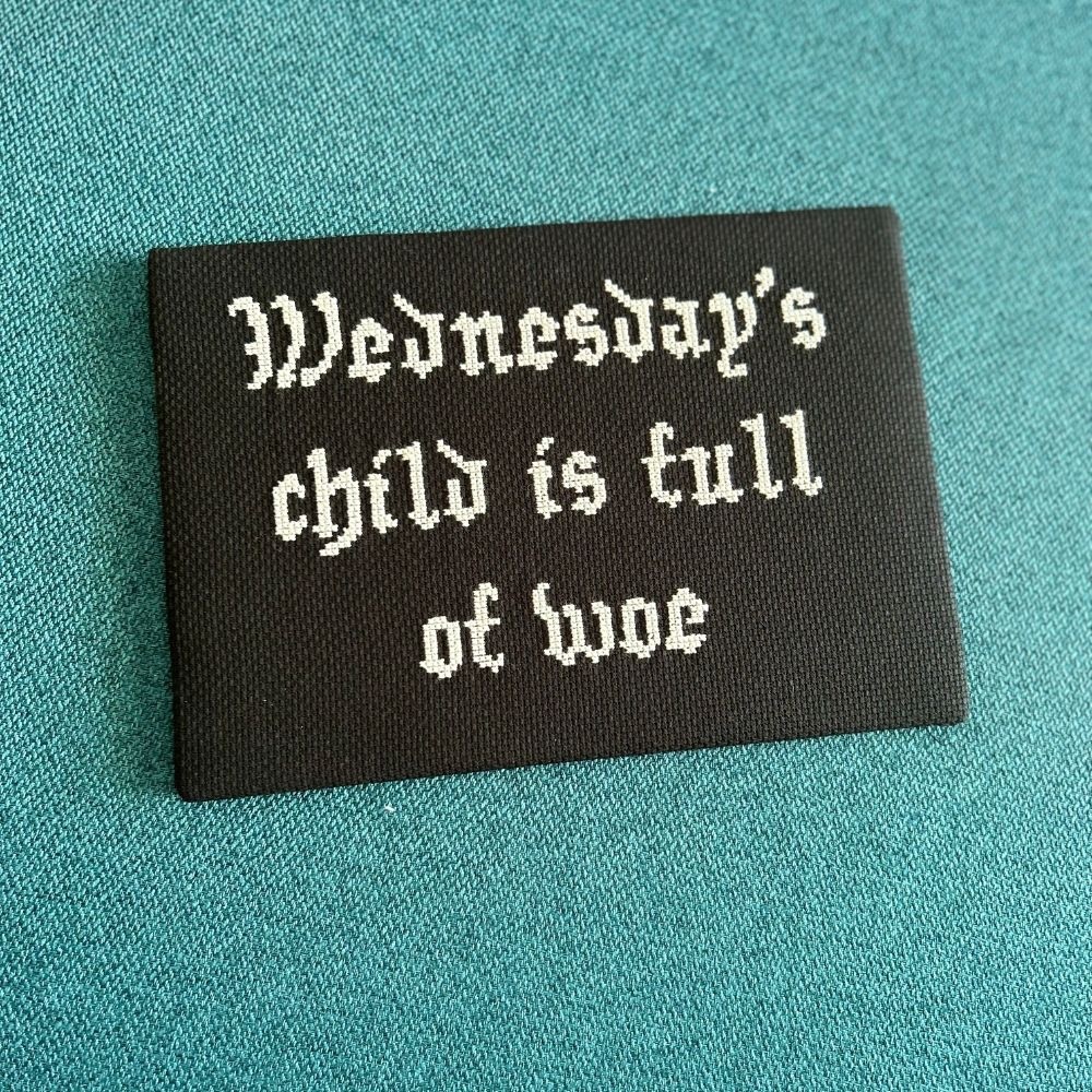 cross stitch of old nursery rhyme Wednesdays child is full of woe stitched in white thread on black aida fabric