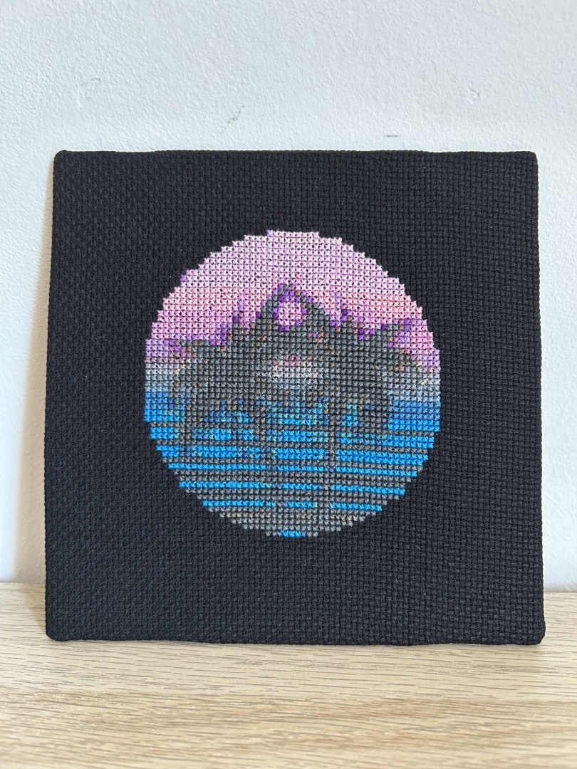 Square cross stitch of two palms with a sunset background in a circular design on black Aida fabric.