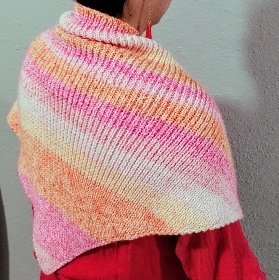 3/4 view from the back of a knitted shawl with self striping yarn, in various shades of pink and orange