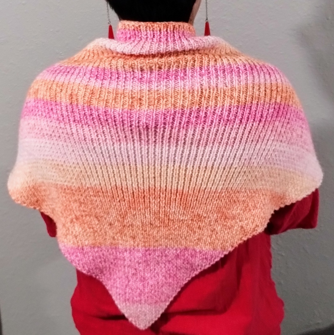 Back view of a knitted shawl with self striping yarn, in various shades of pink and orange