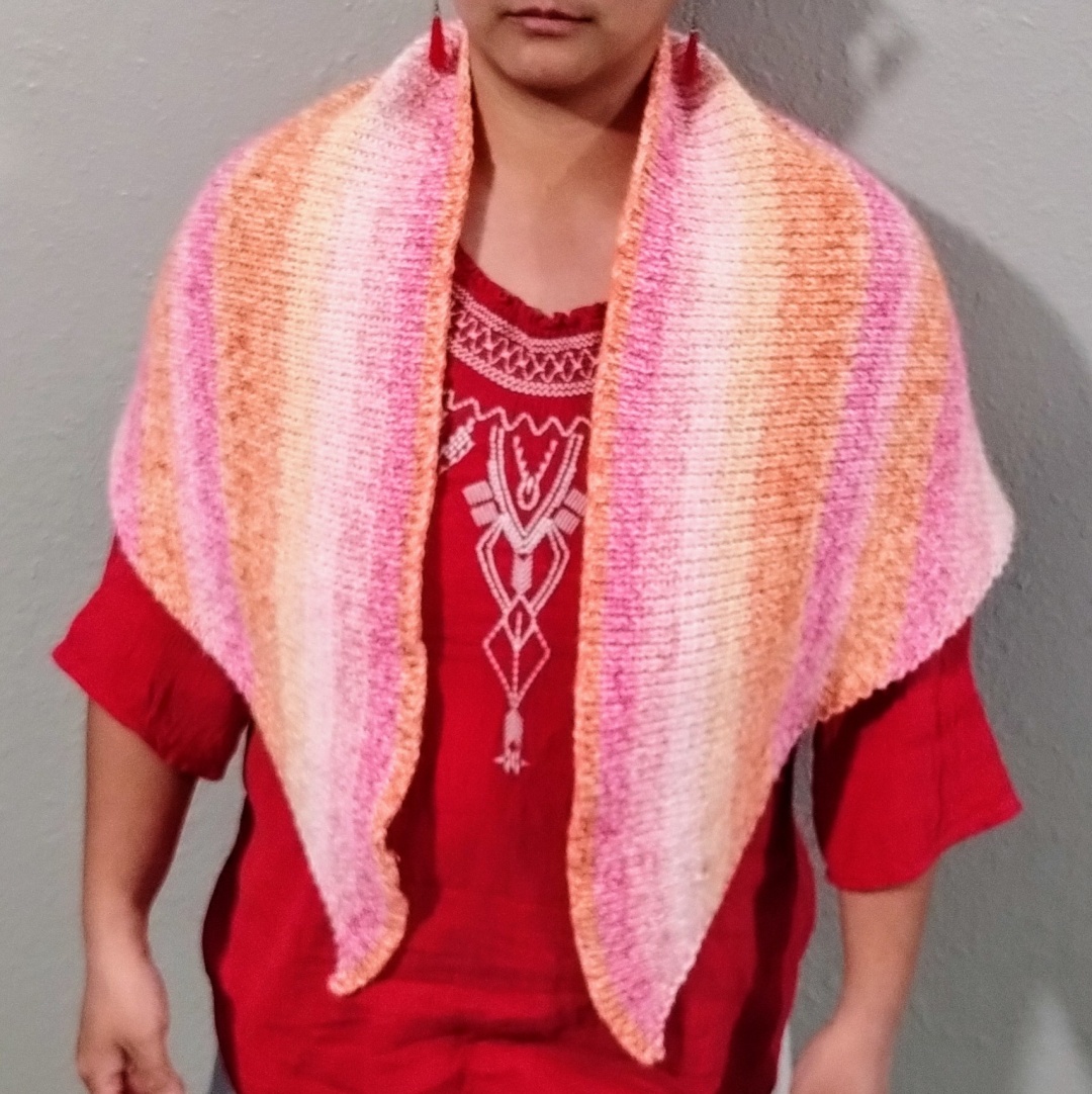 Front view of a knitted shawl with self striping yarn, in various shades of pink and orange.