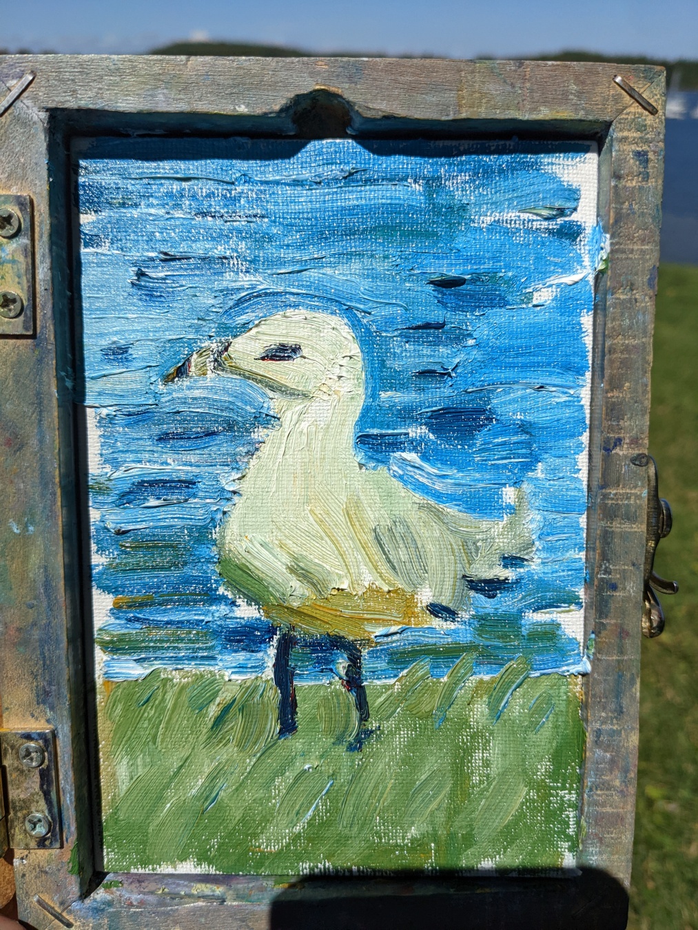 a small painting of a seagull, dirty white against blue water and green grass. The brushstrokes are large and rough.