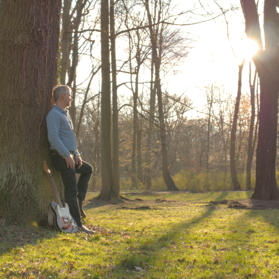 An alternative cover shot for the upcoming EP Simplicity by Andy Robson & The Urban Fox Network. Andy is leaning on a tree in a parc. His guitar leaning beside him. He is looking into the sun, which gives the scene a soft and warm atmosphere.