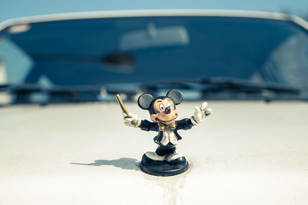 Auf einem weißen VW Käfer steht als Kühlerfigur eine Mickey Maus aus dem "Zauberlehrling". Auf einem weißen VW Käfer steht als Kühlerfigur eine Mickey Maus aus dem "Zauberlehrling".