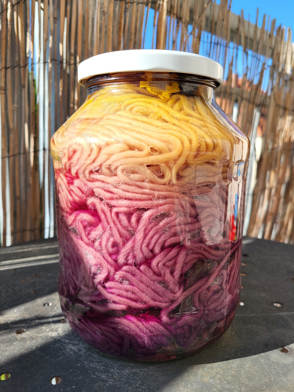 A mason jar full of yarn that looks like yarn pasta. The bottom two third is in a pink purplish colour and the upper top third has a bright yellow tone.