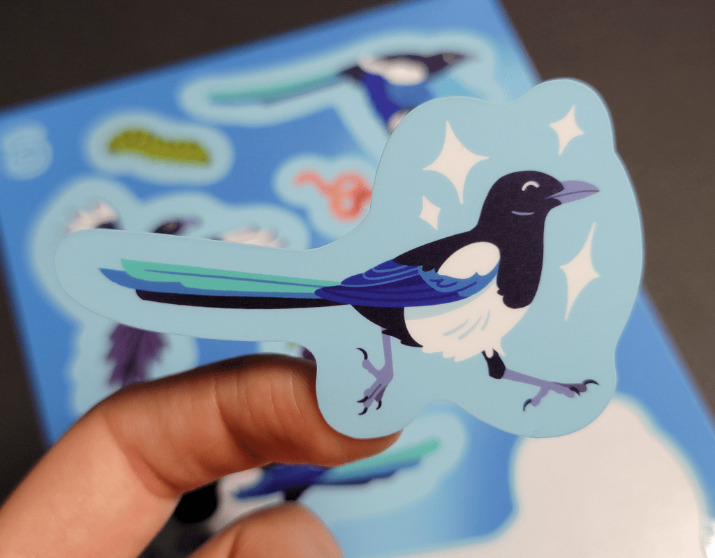 A close up of one of the illustrations of magpies from the previous sheet. The magpie is hopping to the right, both legs in the air, surrounded by white sparkles.