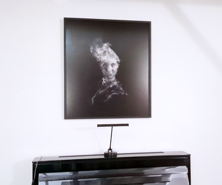 A black and white image based on a portrait pinhole photograph, layered with textures and digitally created smoke, hanging above a piano.