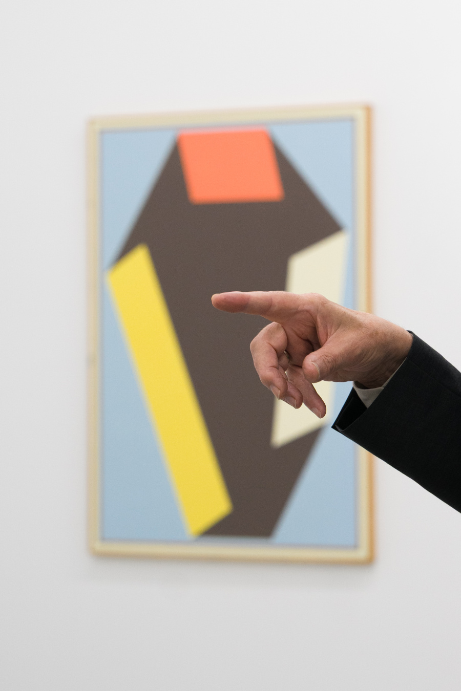 The photo shows the artist Leon Wuidar, whose hand gestures towards one of his abstract paintings in the background – clear shapes and colors become a visible dialogue between painting and movement.